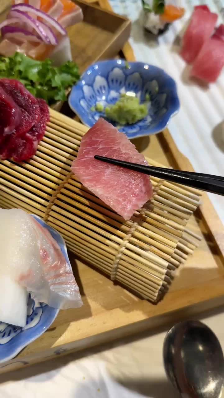 집게로 참치회를 집어 올리는 모습, 뒤편으로 다양한 회와 곁들임 재료들이 보인다.